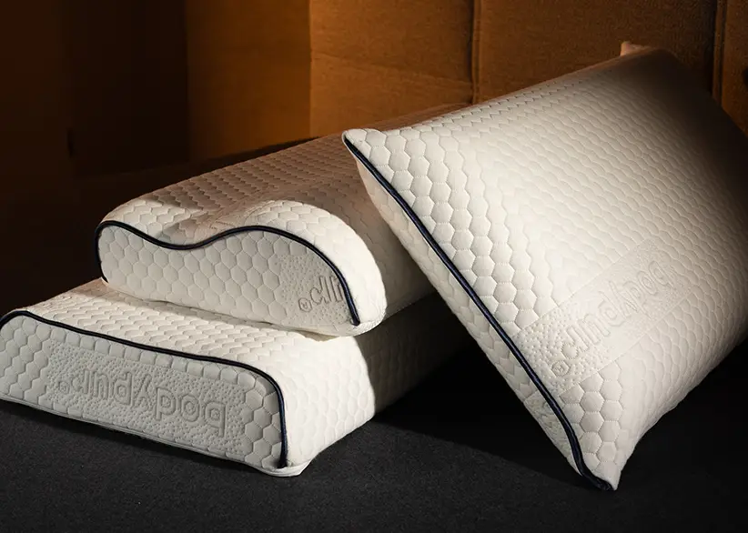 Ein gewelltes und ein flaches Bodypur-Kissen auf einem dunklen Hintergrund, das Design und die Prägung des Bezugs sind gut erkennbar.